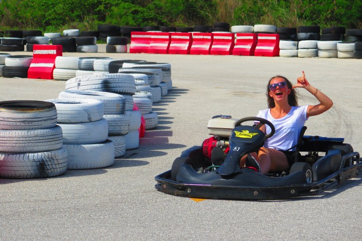 A woman throwing up the shaka sign while driving a go-kart