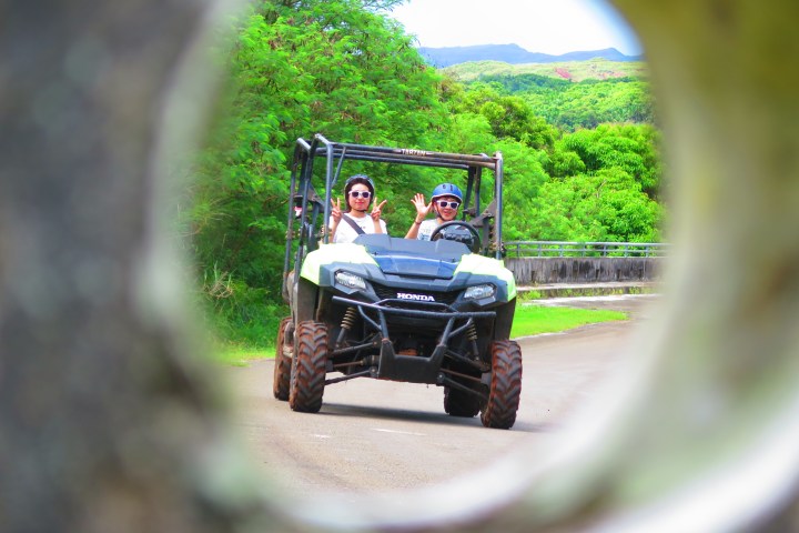 Two people driving a Honda ATV on a road, seen through a circular frame.