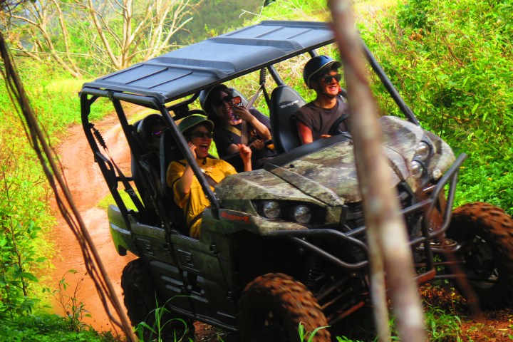Three people riding an off-road vehicle on a grassy trail.