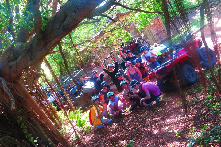Group with helmets gathers near parked off-road vehicles in a sunlit forest.