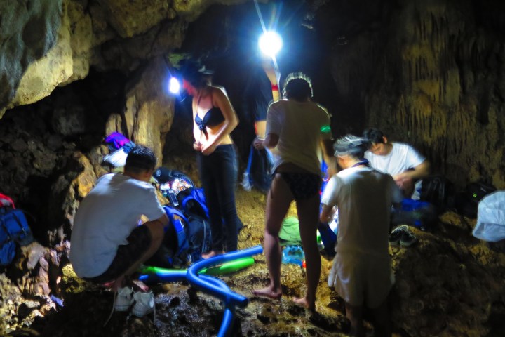 People in a dimly lit cave with headlamps, preparing equipment.