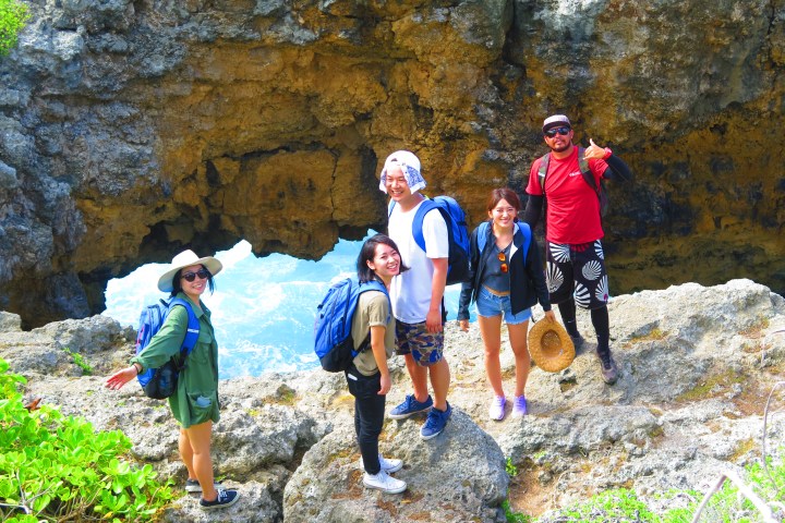 Group of five hikers posing by rocky coastal arch.