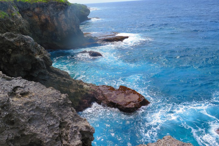 Rocky coastline with blue ocean and waves splashing against cliffs.