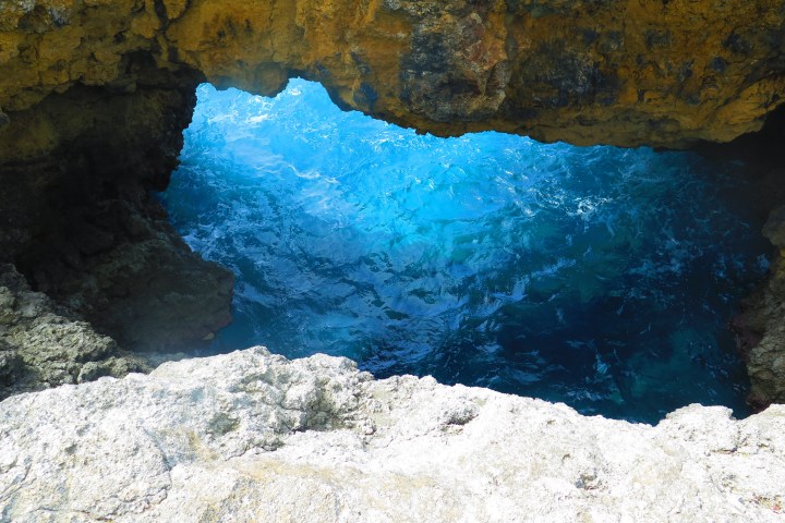 View through rocky archway to bright blue ocean water below.