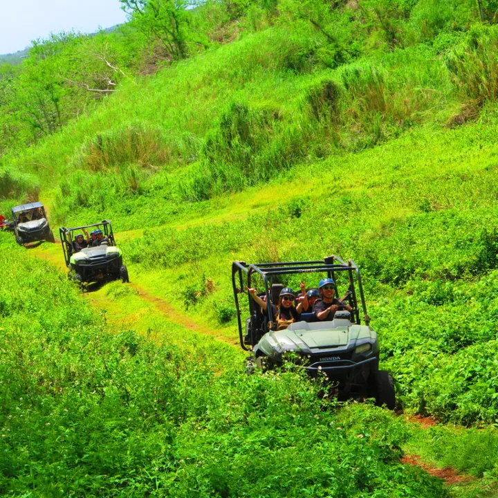Four off-road vehicles driving on a green hillside trail.