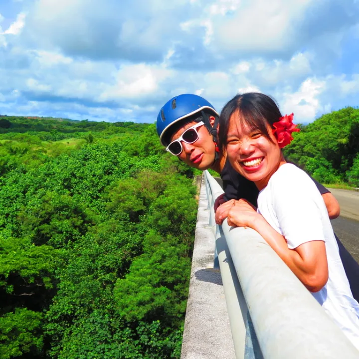 Two people smiling on a bridge with green forest background.