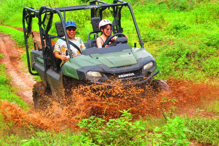 Two people riding an ATV through a muddy path, splashing water and having fun.