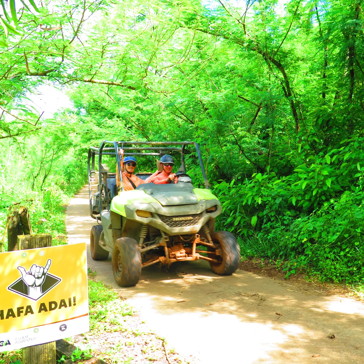 Two people on an ATV on a lush, green forest trail with a 'HAFA ADAI' sign.