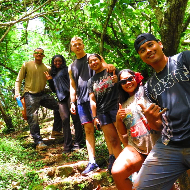 Group of six people smiling on a forest trail with lush greenery.