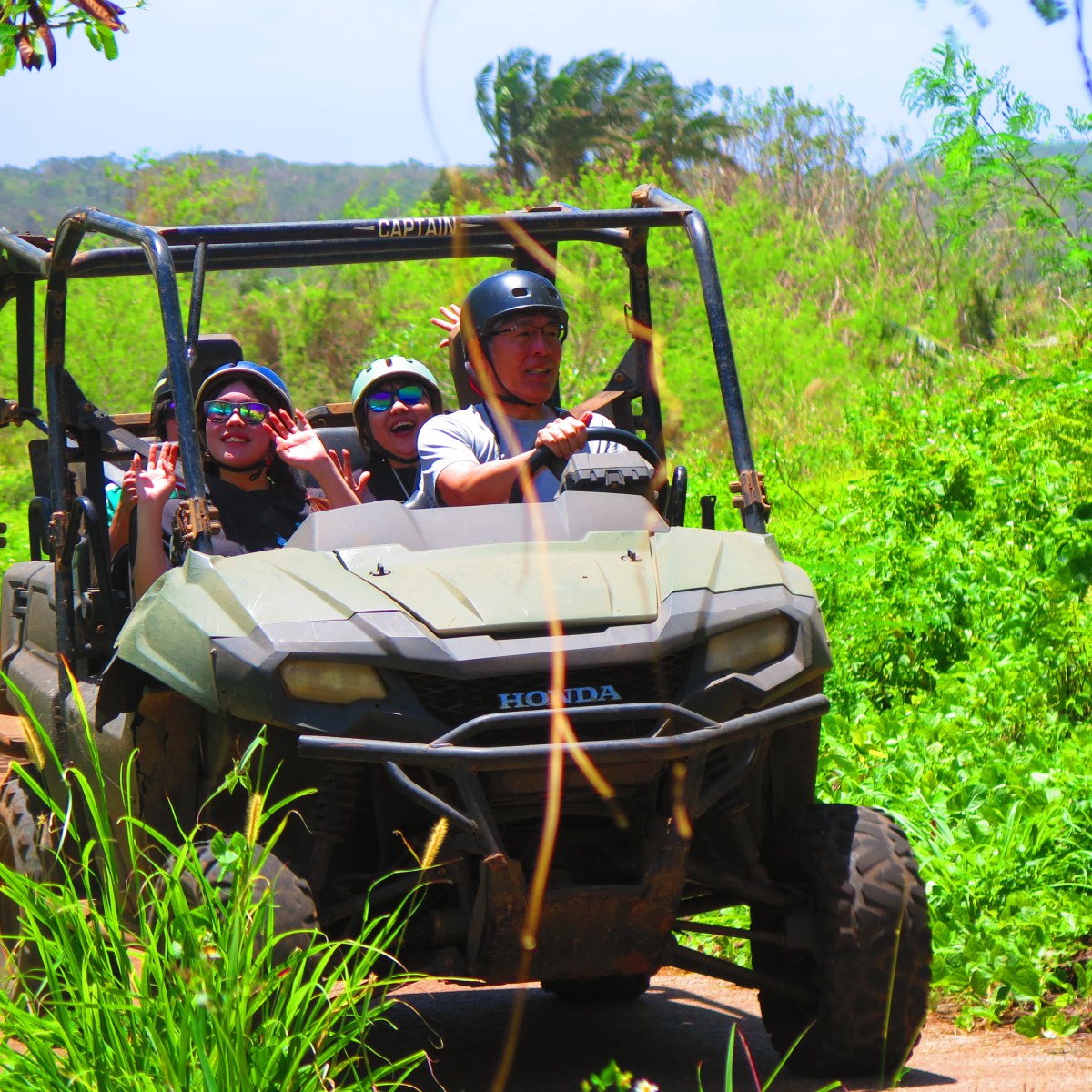 Group of people riding an off-road vehicle on a dirt path in a lush, green setting.