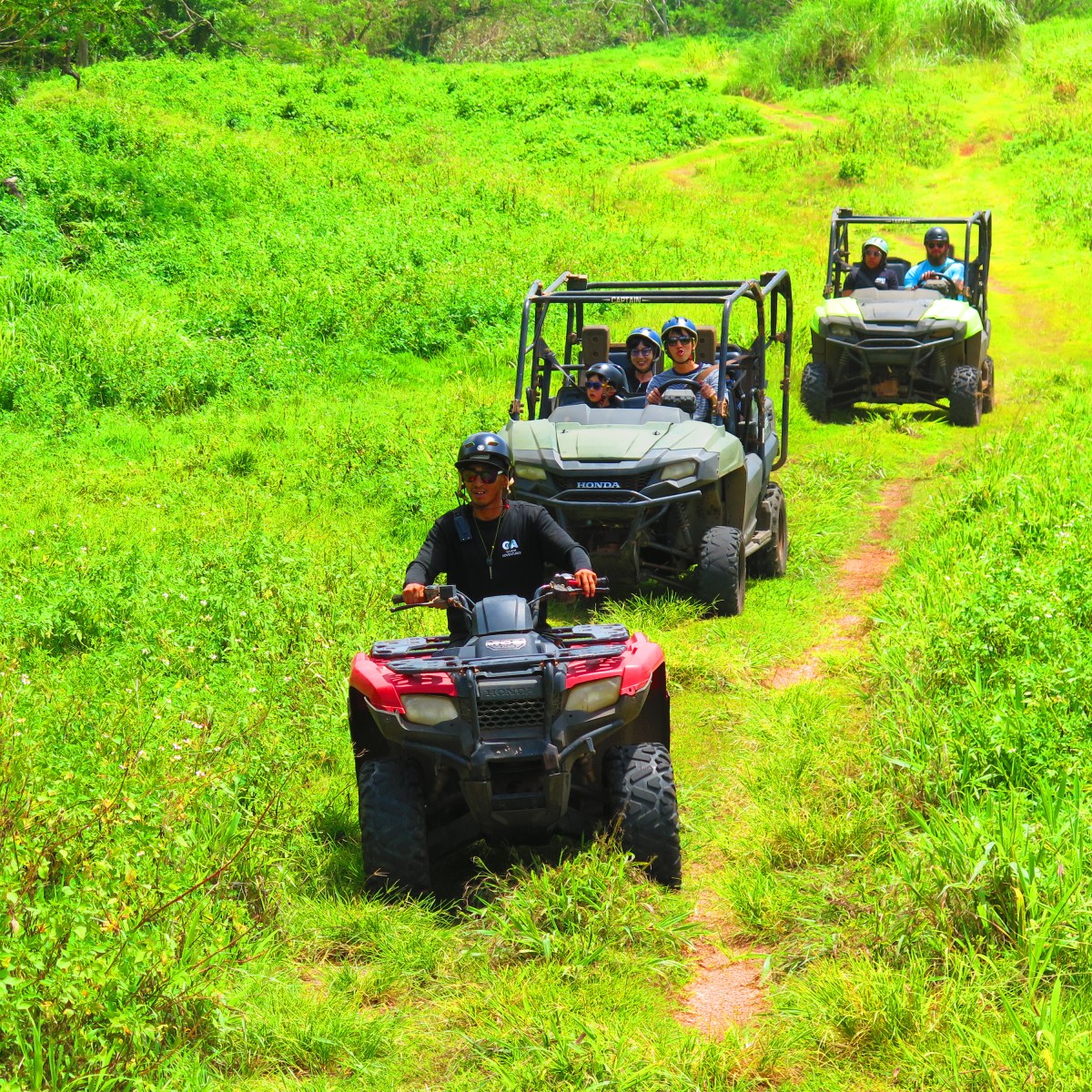 ATVs driving on a grassy trail with people wearing helmets.