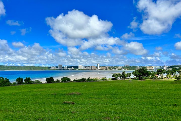a large green field with clouds in the sky