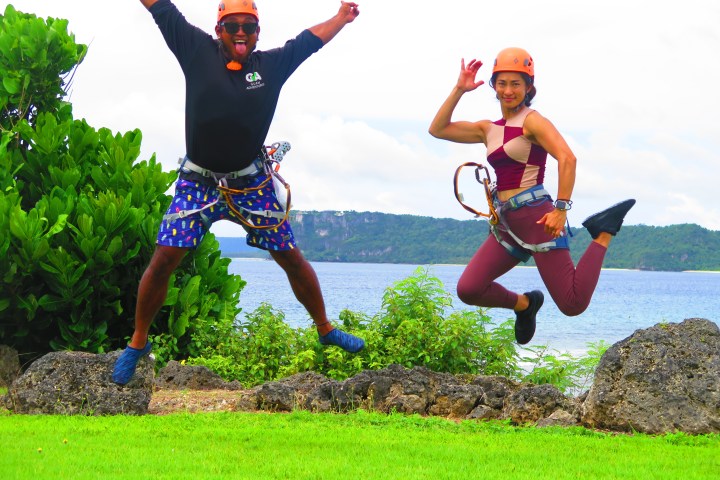 Two people jumping in harnesses by a lake, wearing helmets and safety gear.