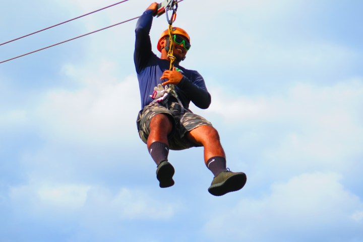 Person ziplining with a helmet against a blue sky.