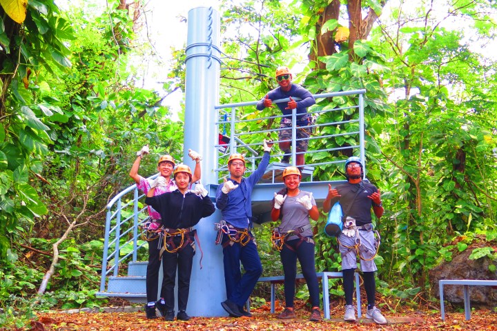 Group of people in helmets and harnesses posing on a platform in a forest.