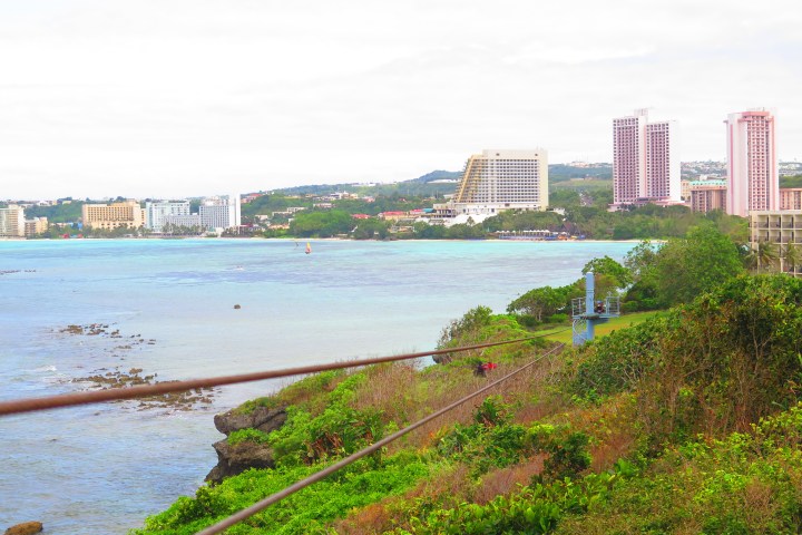 Coastal cityscape with buildings, greenery, and water.