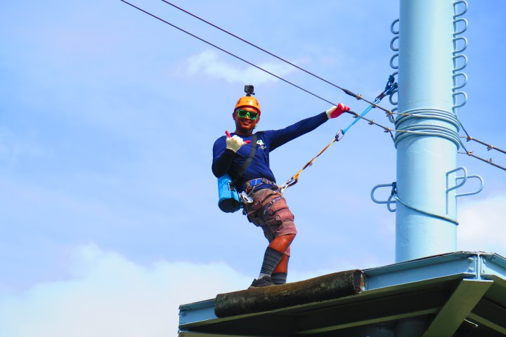 Worker in safety gear on tower, sky background.