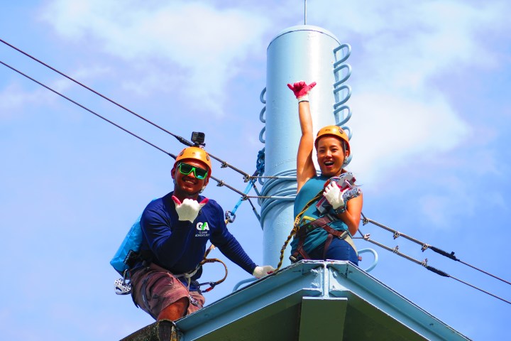 Two people in safety gear cheering on a rooftop near cables.