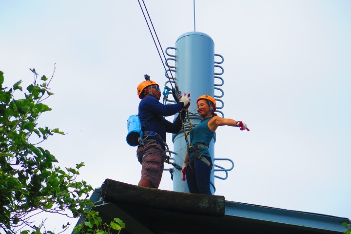 Two people in helmets on a rooftop, securing cables.