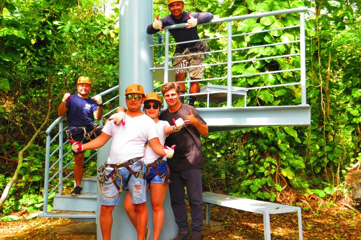 Group of five people in helmets and harnesses posing by metal spiral staircase in forest.